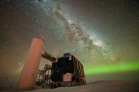 Eine Forschungsstation am Südpol. Man sieht einen sternenreichen Himmel und Polarlichter.