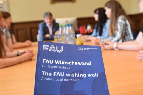Universitätsleitung sitzt mit Studierenden und Diversitybeauftragten an Tisch und bespricht Wünsche aus der Kampagne Wünschewand. Im Vordergrund die Broschüre.