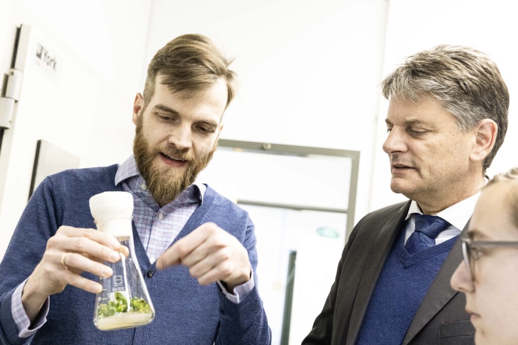 FAU Professor Fuhrmann hat einen Glaskolben in der Hand und erklärt FAU Präsident Hornegger seine Forschung. 