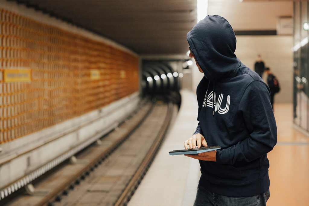 Mann mir Kapuzenpullover und hochgezogener Kapuze steht am U-Bahngleis.