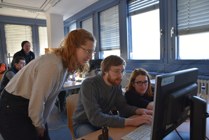 Zwei Studentinnen und ein Student arbeiten fröhlich.