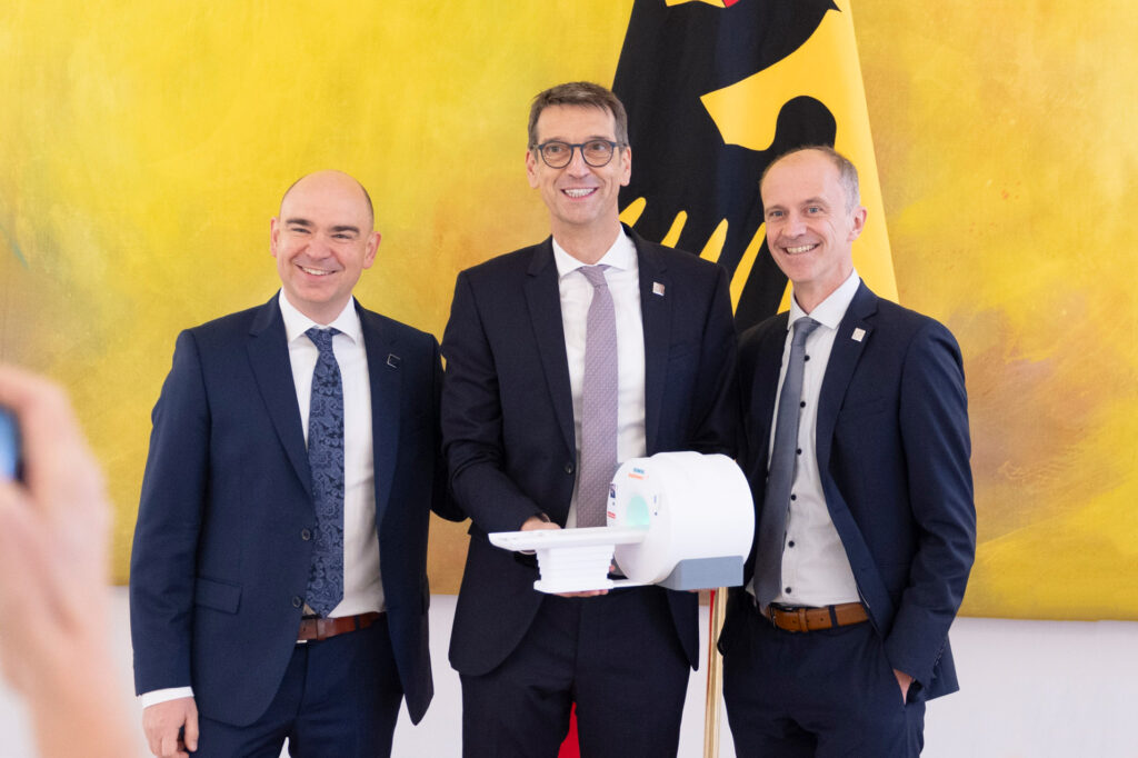 Die drei Zukunftspreis-Gewinner 2023 Prof. Dr. Michael Uder (Uniklinikum Erlangen), Dr. David Grodzki (l.) und Dr. Stephan Biber (r., beide Siemens Healthineers) mit dem Modell des Niederfeld-MRTs, das bald in Peru den Betrieb aufnehmen wird.