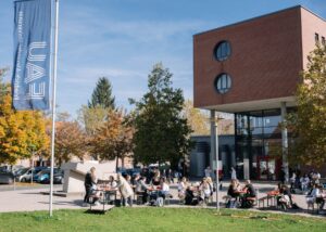 Die WiSo in Nürnberg. Vor dem Gebäude sitzen Studierende auf Bierbänken.