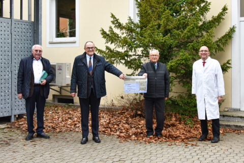 Vier Männer stehen nebeneinander und eine Spende wird überrreicht.