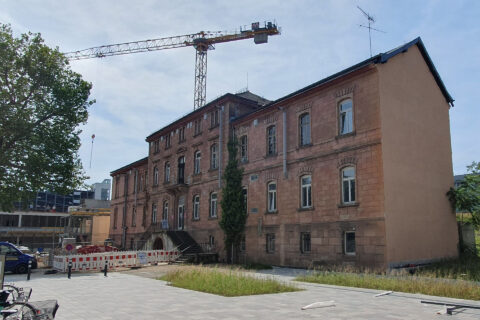 Bilder der ehemaligen Heil- und Pflegeanstalt in Erlangen. Hinter dem roten Gebäude steht ein Baukran.