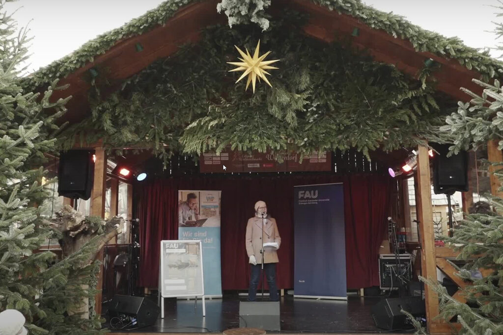 FAU-Prof. Salo auf dem Weihnachtsmarkt auf einer Bühne die an eine Krippe erinnert. Über ihr ein großer Weihnachtsstern.