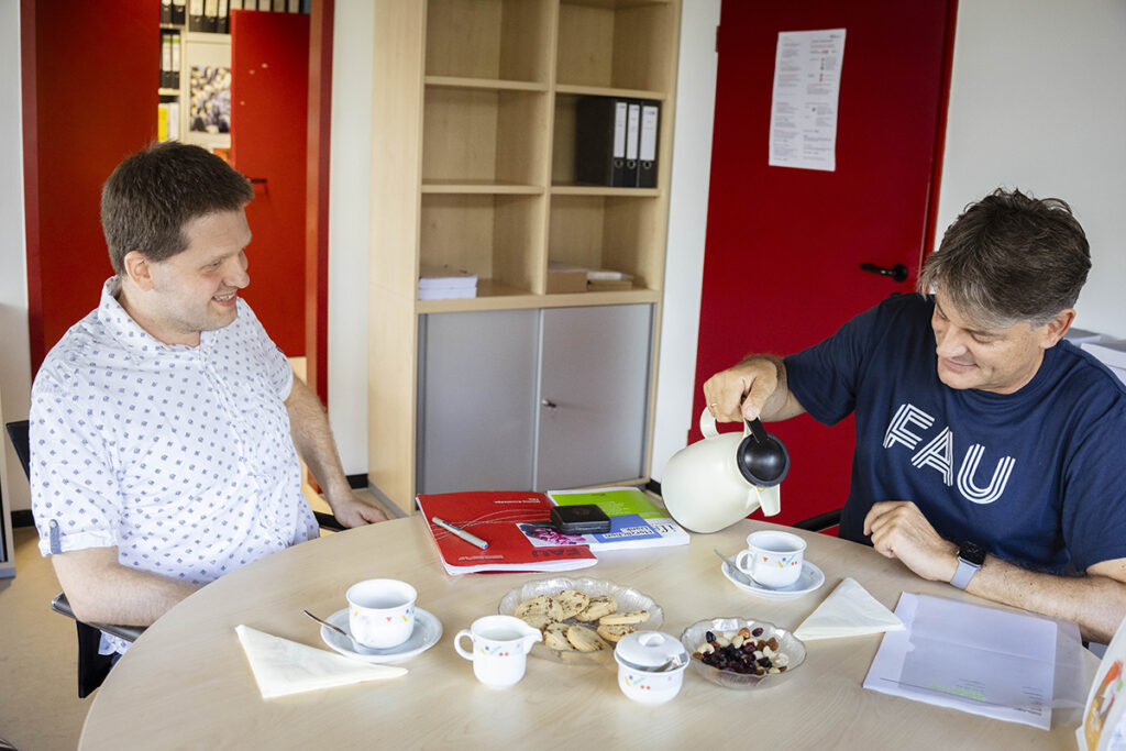 Prof. Hechtner and FAU-Präsident Hornegger sitting at a table. Hornegger is pouring himself a coffee, and Hechtner is sitting next to him. 