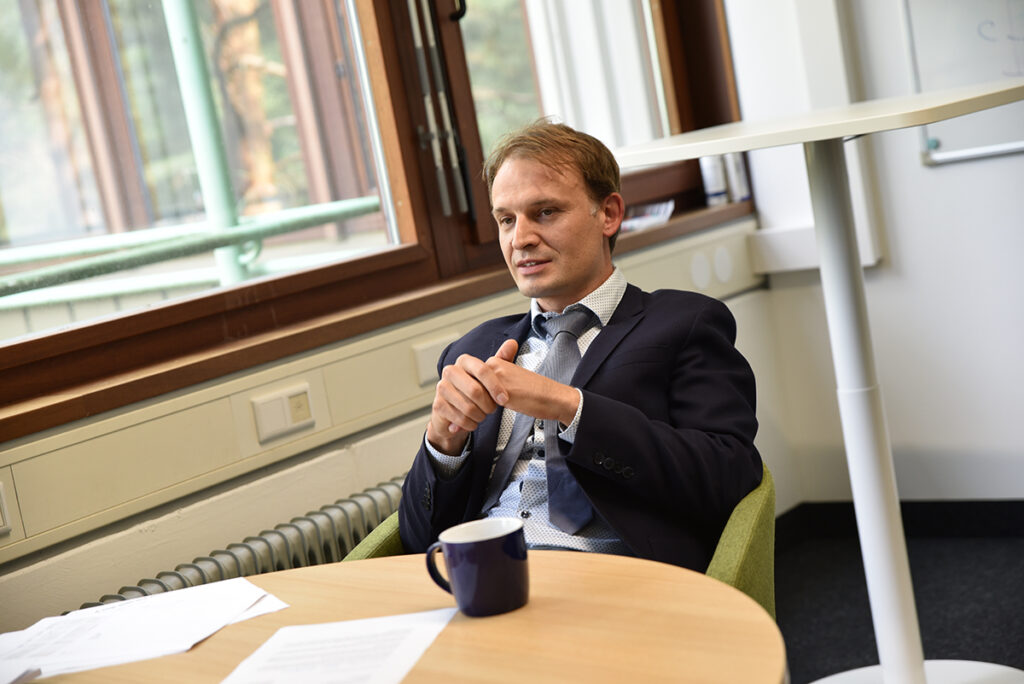 Christopher Eichler sitzt an einem Tisch mit einer FAU Tasse vor sich. 