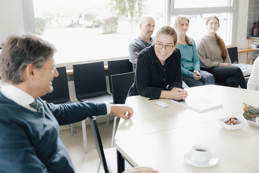 FAU-Präsident Joachim Hornegger besucht Prof. Dr. Caroline Voskens, Professur für Translationale Immundermatologie, in ihrem Labor. Sie sitzen gemeinsam an einem Tisch und unterhalten sich. Voskens lächelt. 