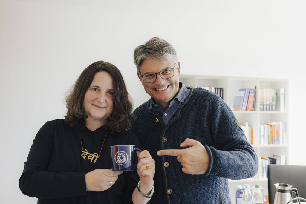 Prof. Lillge mit einer FAU Kaffeetasse, Hornegger zeigt auf die Tasse und grinst.